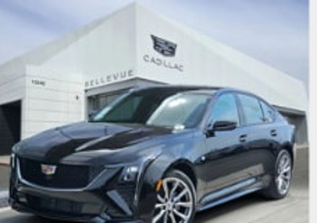 Black Cadillac CT5 parked in front of a Cadillac dealership showroom